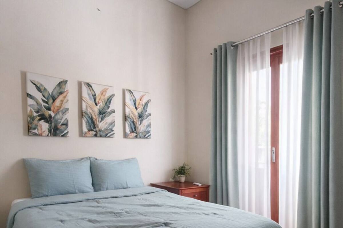A bedroom with a bed, a nightstand, a wall-mounted air conditioner, and a window with curtains.