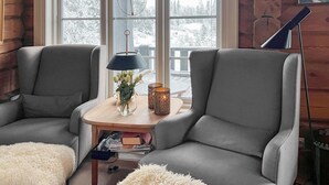 Un rincón acogedor con dos sillones grises, una mesita de madera con lámpara, velas y un jarrón de flores.