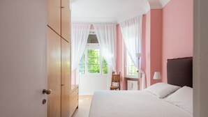A bedroom with a bed, a chair, a desk, and a window with curtains.