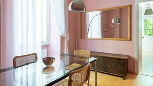 A room with a glass table, two wicker chairs, a wooden cabinet, and a large mirror on the wall.