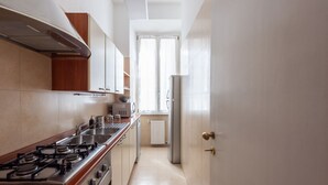 A narrow kitchen with a gas stove, oven, and a refrigerator.