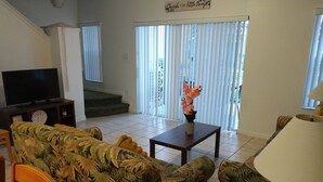 A living room with a sofa, a coffee table, a TV, and a lamp. There is a staircase leading to another level. - Adorable Townhouse at Magic Resort no fees-1064 (Kissimmee)