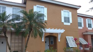 A residential building with a beige exterior, white shutters, and a small porch. - Adorable Townhouse at Magic Resort no fees-1064 (Kissimmee)