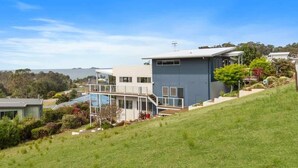 A modern two-story house with a balcony, a swimming pool, and a hilly landscape in the background. - Three Sisters | Ocean Views & Walk to Beach (Long Beach)