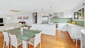 A modern kitchen with white cabinetry, a glass dining table, and a green backsplash. - Three Sisters | Ocean Views & Walk to Beach (Long Beach)