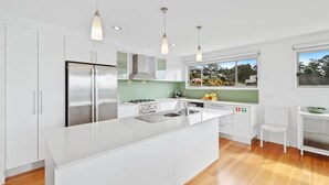 A modern kitchen with white cabinetry, stainless steel appliances, a large island, pendant lighting, and a view through a window. - Three Sisters | Ocean Views & Walk to Beach (Long Beach)