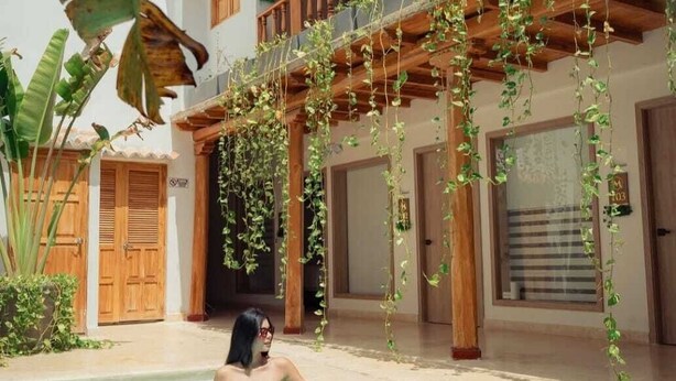 Una mujer en una piscina con un balcón de madera y plantas colgantes.