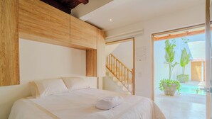 Un dormitorio con una cama grande, cabecera de madera y vistas a una piscina y plantas.