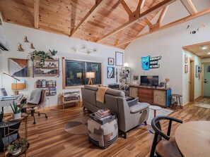 A modern living room with a wooden ceiling, a grey sofa, a coffee table, and a TV. - Private Forest Retreat • Spa Bath • Near the Coast • Central Midcoast Hub (Searsport)