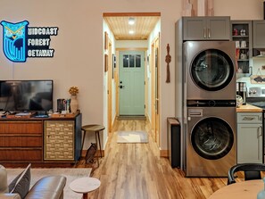 A modern kitchen with a built-in washer and dryer, wooden flooring, and a flat-screen TV. - Private Forest Retreat • Spa Bath • Near the Coast • Central Midcoast Hub (Searsport)