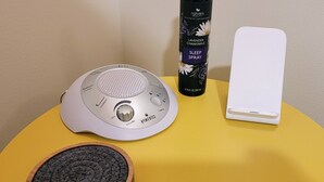 A white portable speaker, a lavender chamomile spray bottle, and a white charging dock on a yellow surface. - Private Forest Retreat • Spa Bath • Near the Coast • Central Midcoast Hub (Searsport)