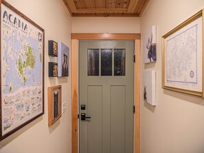 A hallway with a green door, framed maps, and artwork on the walls. - Private Forest Retreat • Spa Bath • Near the Coast • Central Midcoast Hub (Searsport)