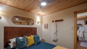 A hotel room with a wooden ceiling, a bed with blue and yellow bedding, a bedside table, a mirror, and a wall-mounted robe rack. - Private Forest Retreat • Spa Bath • Near the Coast • Central Midcoast Hub (Searsport)