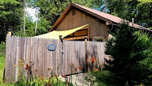 A wooden cabin with a metal roof, surrounded by a wooden fence and a sign that reads "Mildcoast Forest Getaway". - Private Forest Retreat • Spa Bath • Near the Coast • Central Midcoast Hub (Searsport)