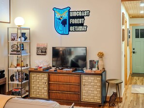 A modern living room with a flat-screen TV, a neon sign, a bookshelf, and a decorative owl statue.