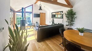 A spacious living area with a high ceiling, wooden beams, a dark sofa, a dining table, and a potted plant. - 1 bedroom accommodation in Llangollen (Llangollen)