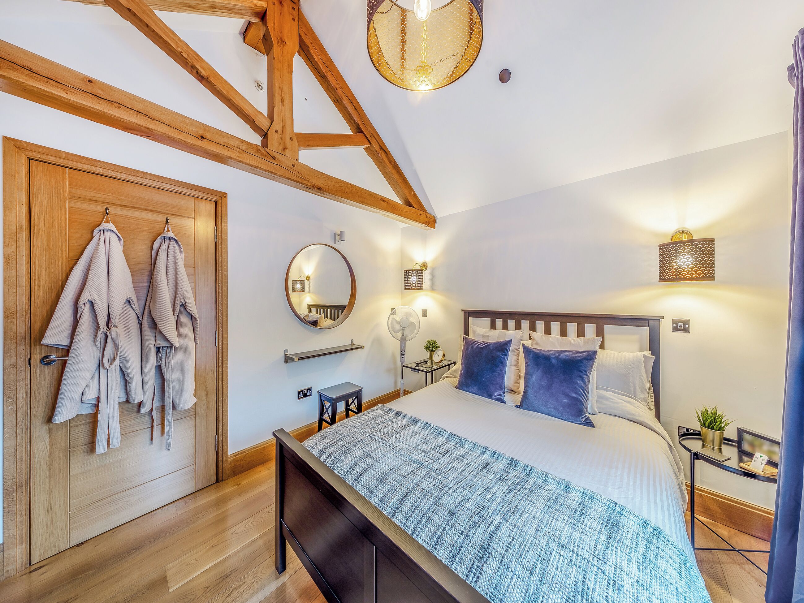 A bedroom with a wooden ceiling, a bed with blue and white bedding, a bedside table with a lamp, and a mirror on the wall.