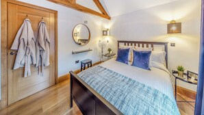 A bedroom with a wooden ceiling, a bed with blue and white bedding, a bedside table with a lamp, and a mirror on the wall. - 1 bedroom accommodation in Llangollen (Llangollen)