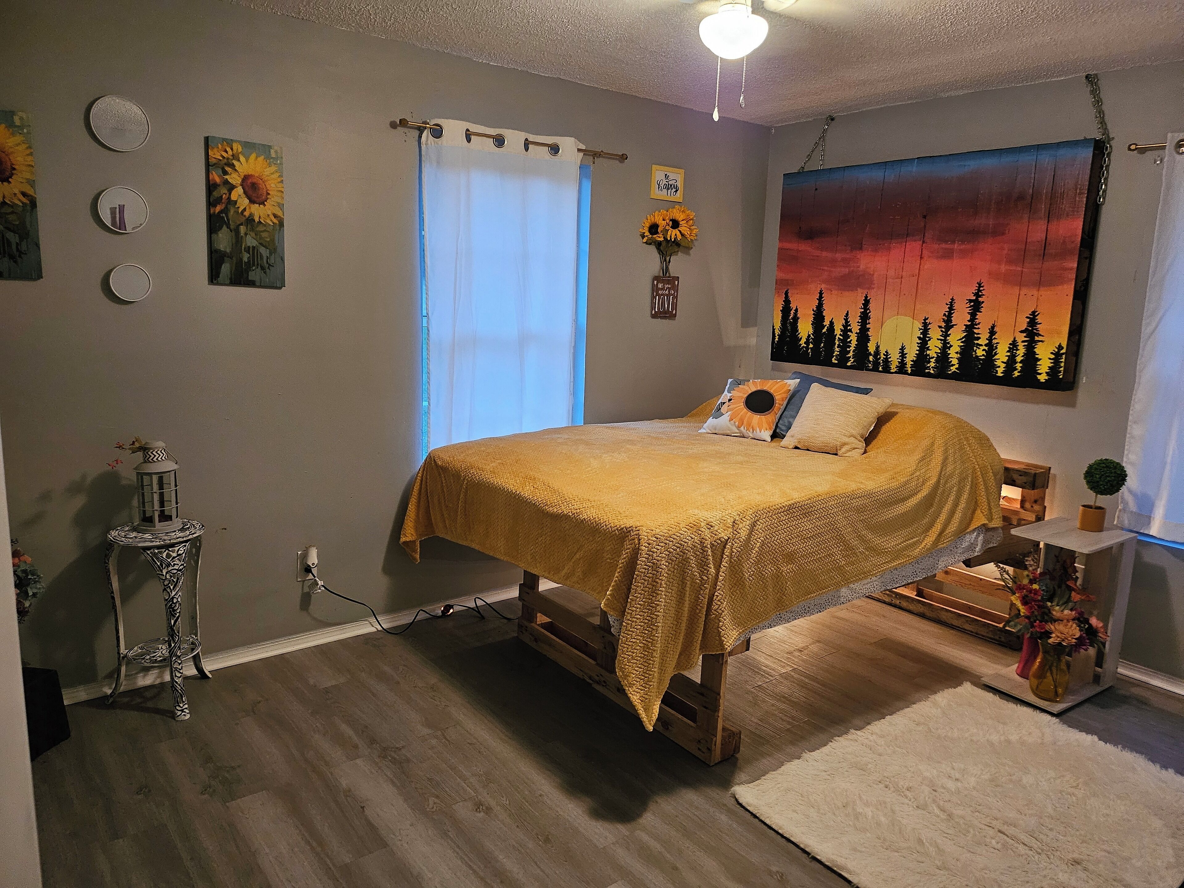 A bedroom with a bed, a nightstand, a lamp, a painting, and a window with curtains.