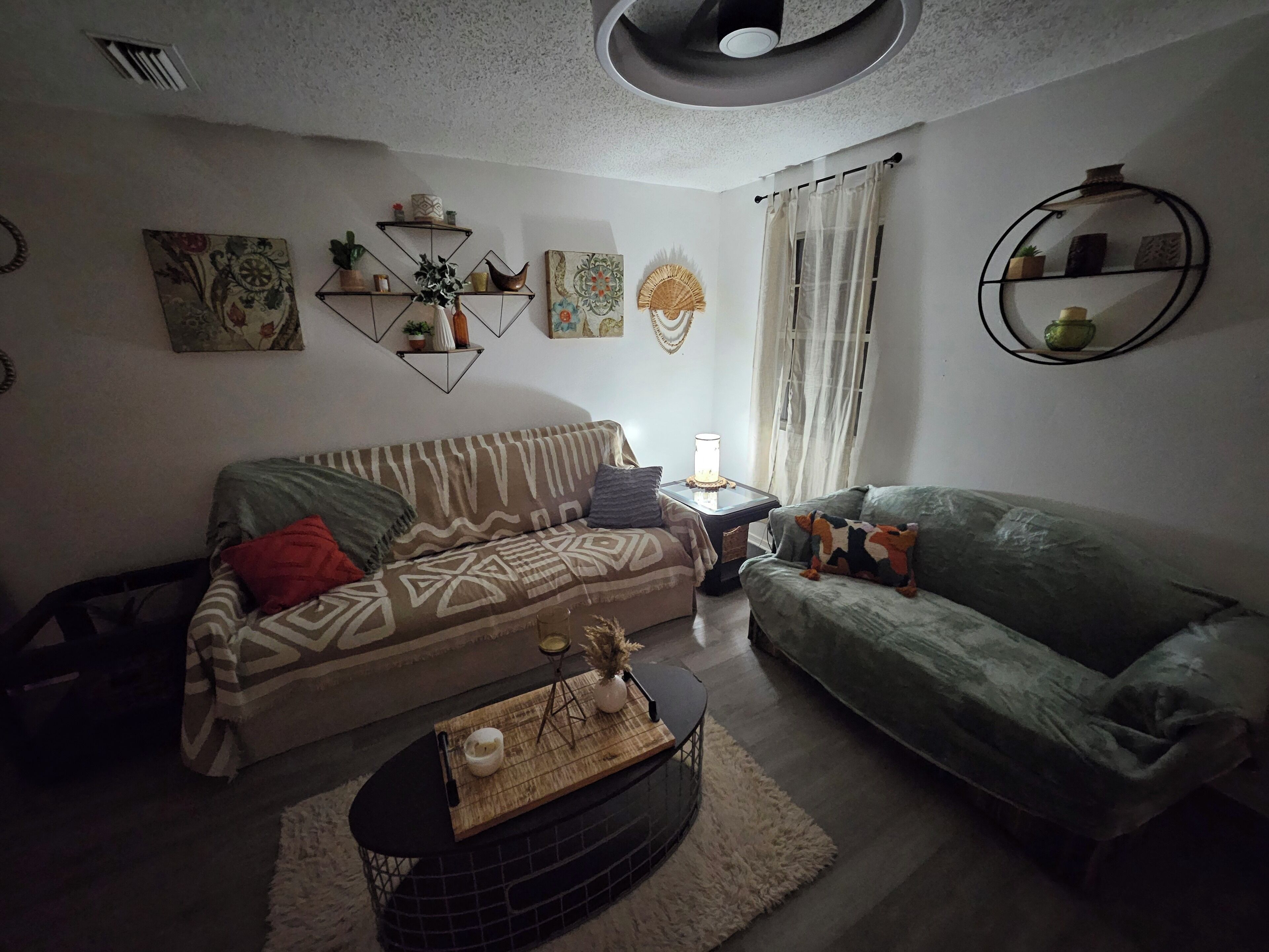 A living room with a patterned sofa, a round coffee table, and decorative items on shelves.