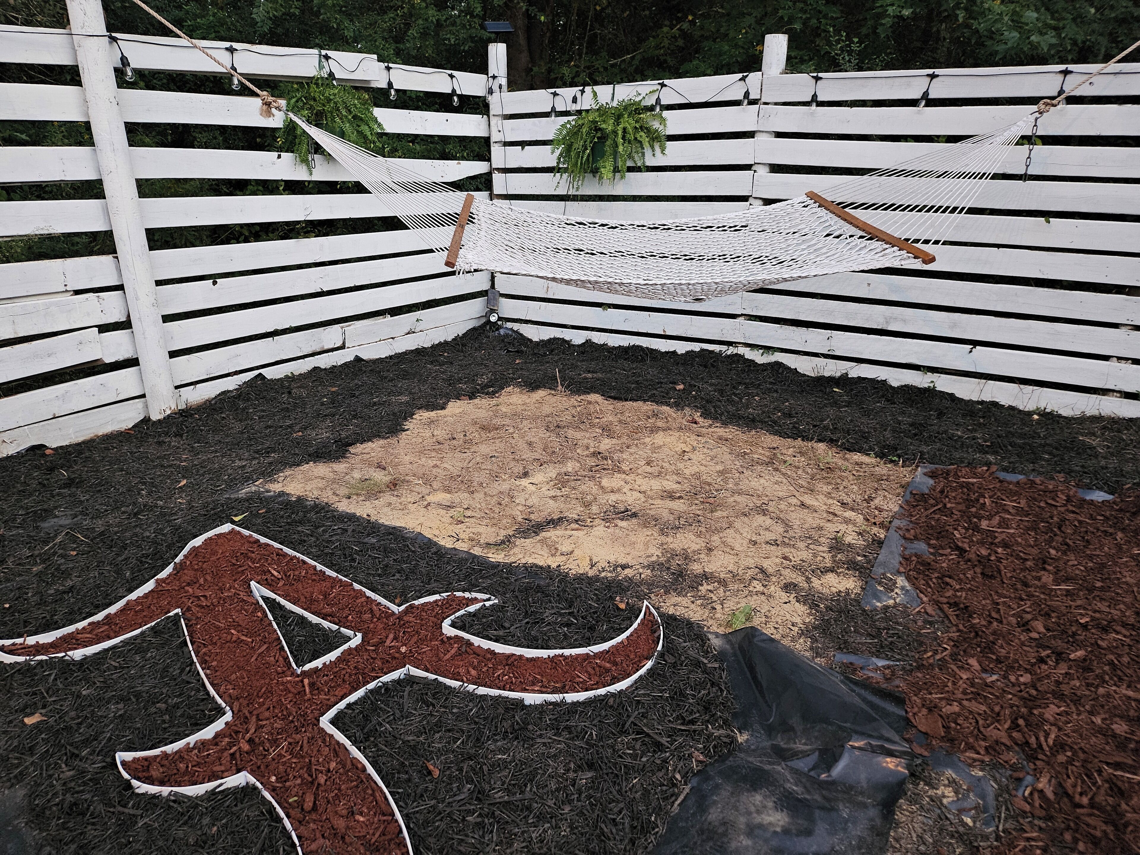 Un jardin clos, aménagé avec un hamac, un paillis et un grand symbole décoratif peint au sol.