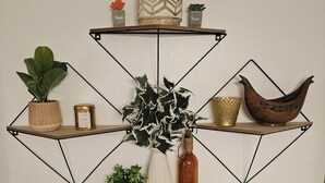 A geometric wall shelf with various decorative items including plants, a candle, and a wooden bowl.