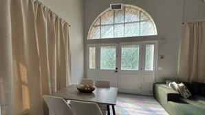 Un coin repas avec une table, des chaises et un récipient rempli d’objets décoratifs. On y trouve également un canapé et une fenêtre à vitrage dépoli.