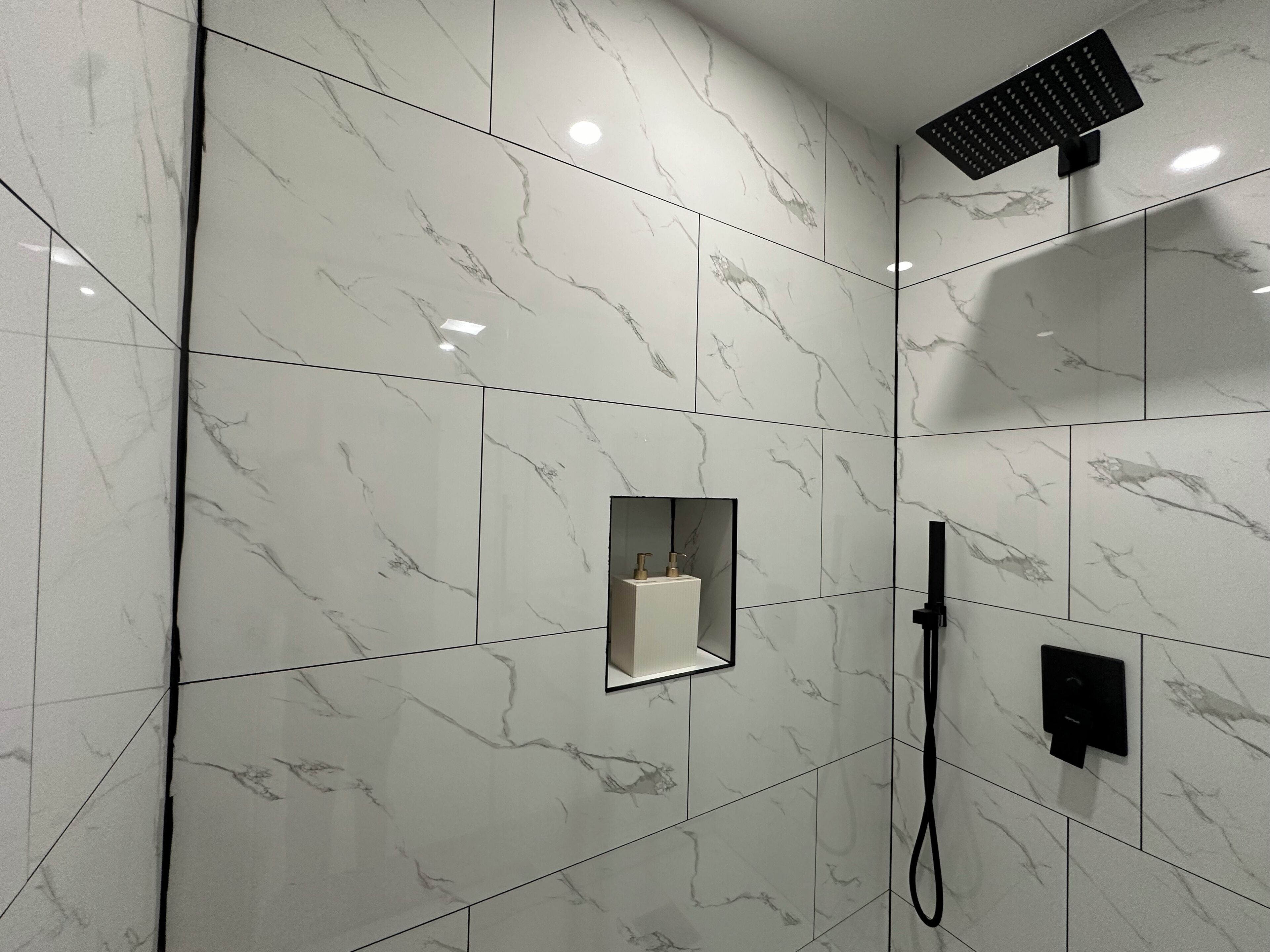 Een moderne badkamer met marmeren tegels, een handdouche en een handdoekdispenser.