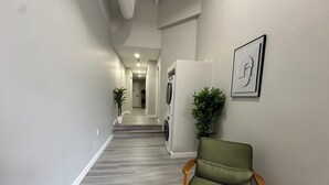 Un couloir avec une chaise verte, un lave-linge et une plante en pot.