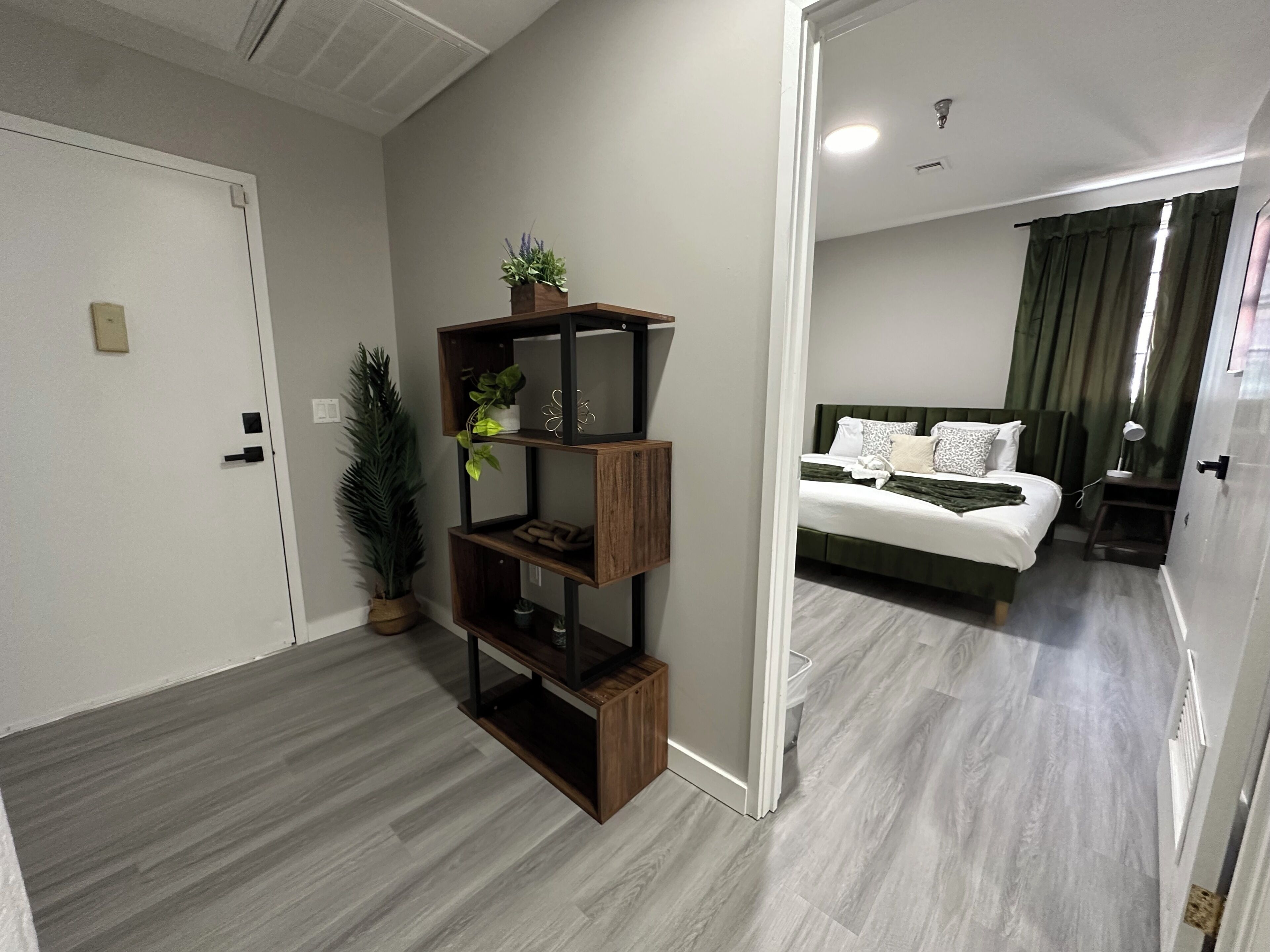 Een moderne hotelkamer met een houten vloer, een inbouwkast, een potplant, een opgemaakt bed en een nachtkastje met een lamp.