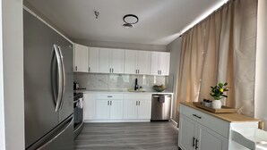 Une cuisine moderne avec des meubles blancs, un réfrigérateur en acier inoxydable et un plan de travail en bois.