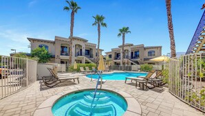 A pool area with lounge chairs, palm trees, and a building with multiple balconies. - Desert Breeze: #244514 1 BR, community pool and spa! (La Quinta)