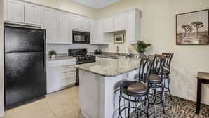A kitchen with white cabinets, a black refrigerator, a microwave, and a stove. There is a bar area with stools. - Desert Breeze: #244514 1 BR, community pool and spa! (La Quinta)