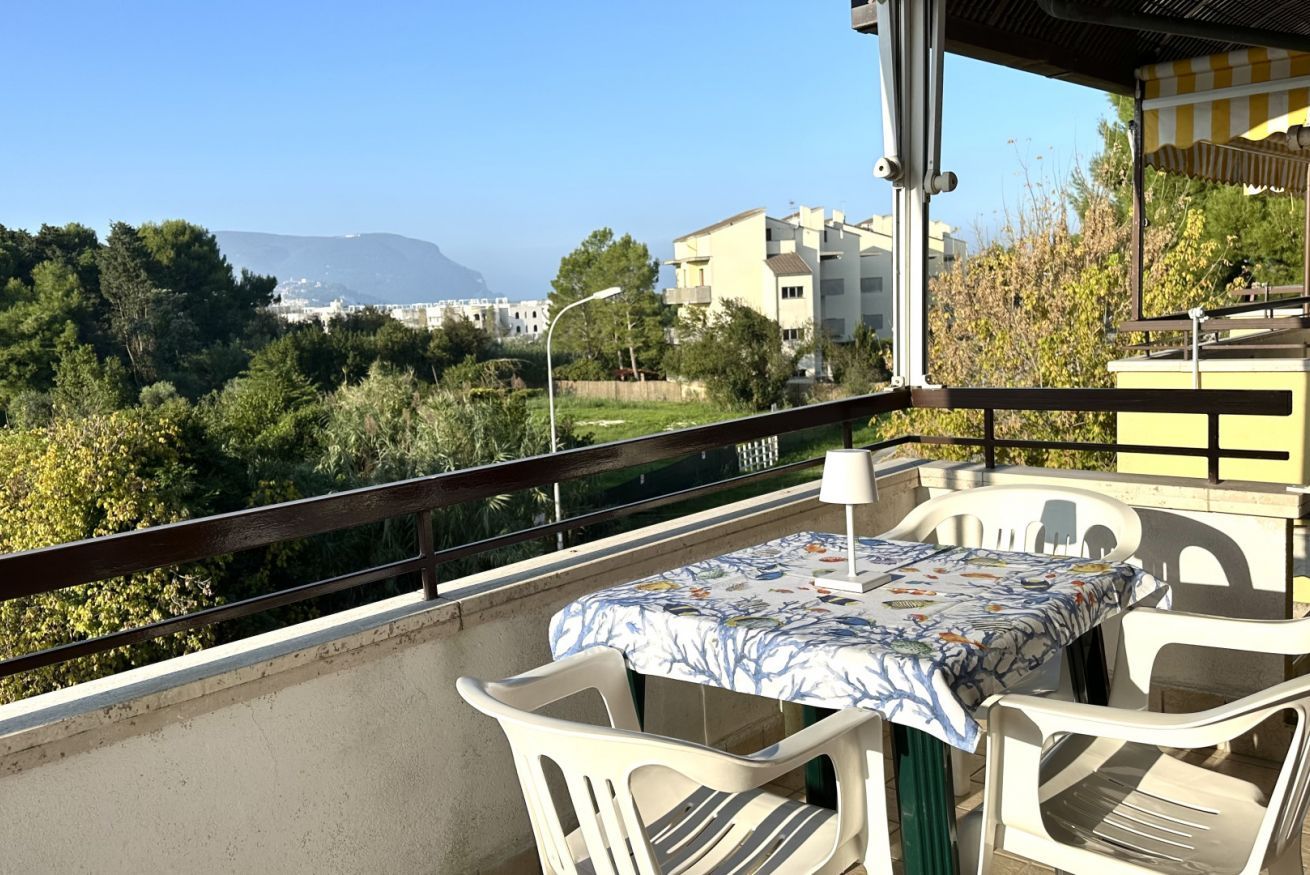 Un balcone con tavolo e sedie, affacciato su un paesaggio montuoso e edifici residenziali.