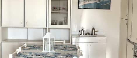 A dining area with a table, chairs, a cabinet with glass doors, a small kitchen counter, and a framed picture on the wall.