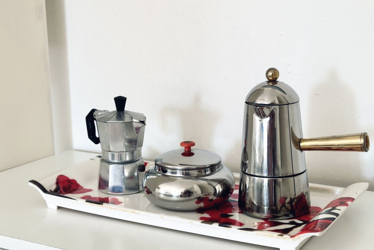Una bandeja con una cafetera, una tetera y un recipiente sobre una superficie blanca.