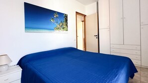 A bedroom with a bed, a nightstand, a wardrobe, and a painting of a beach scene. - M410 - Marcelli, comfortable three-room apartment with large terrace (Marcelli)