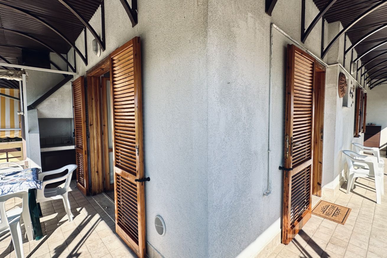 A covered outdoor area with wooden shutters, a table with chairs, and a white wall.