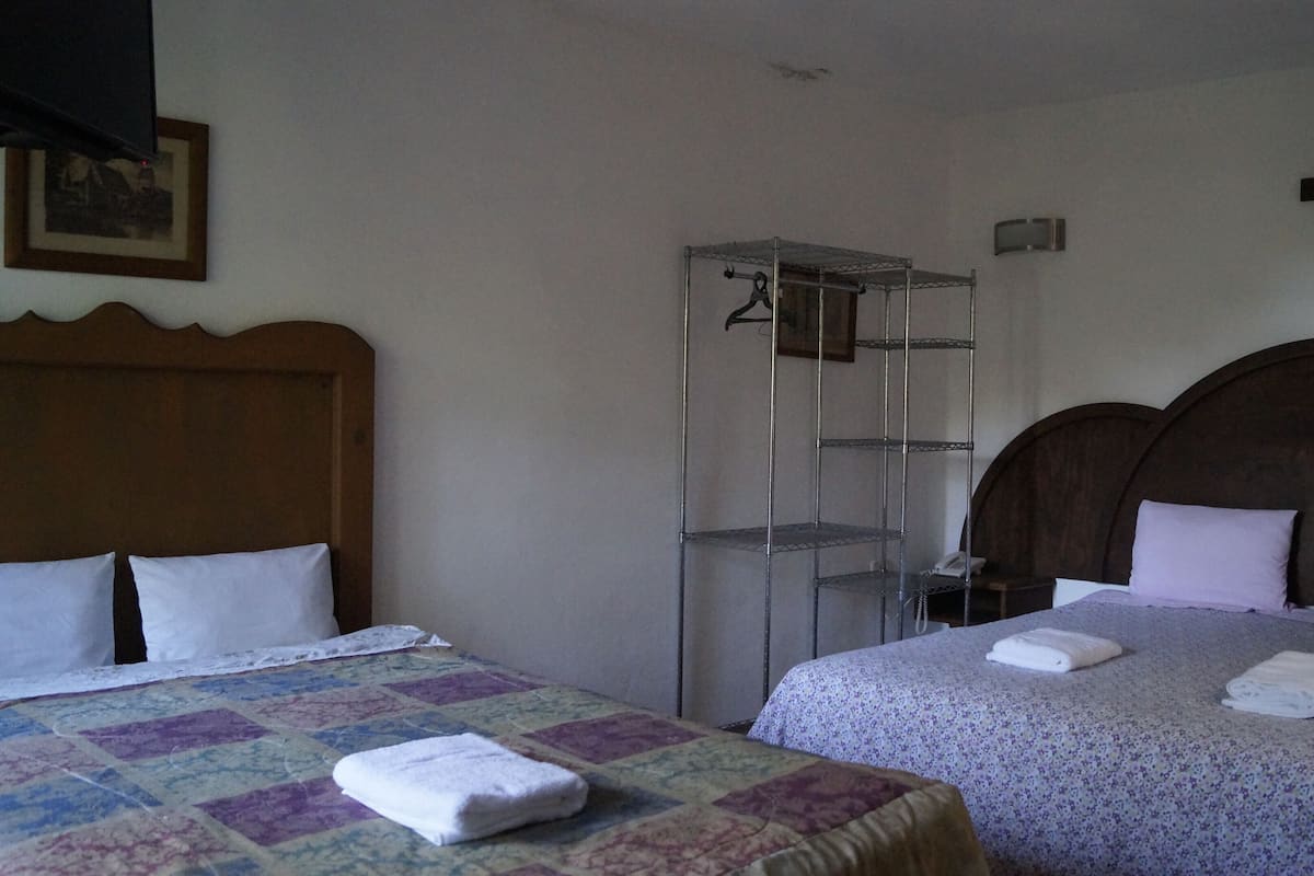 Ett hotellrum med två sängar, en garderob, ett kors på väggen och en inramad tavla.