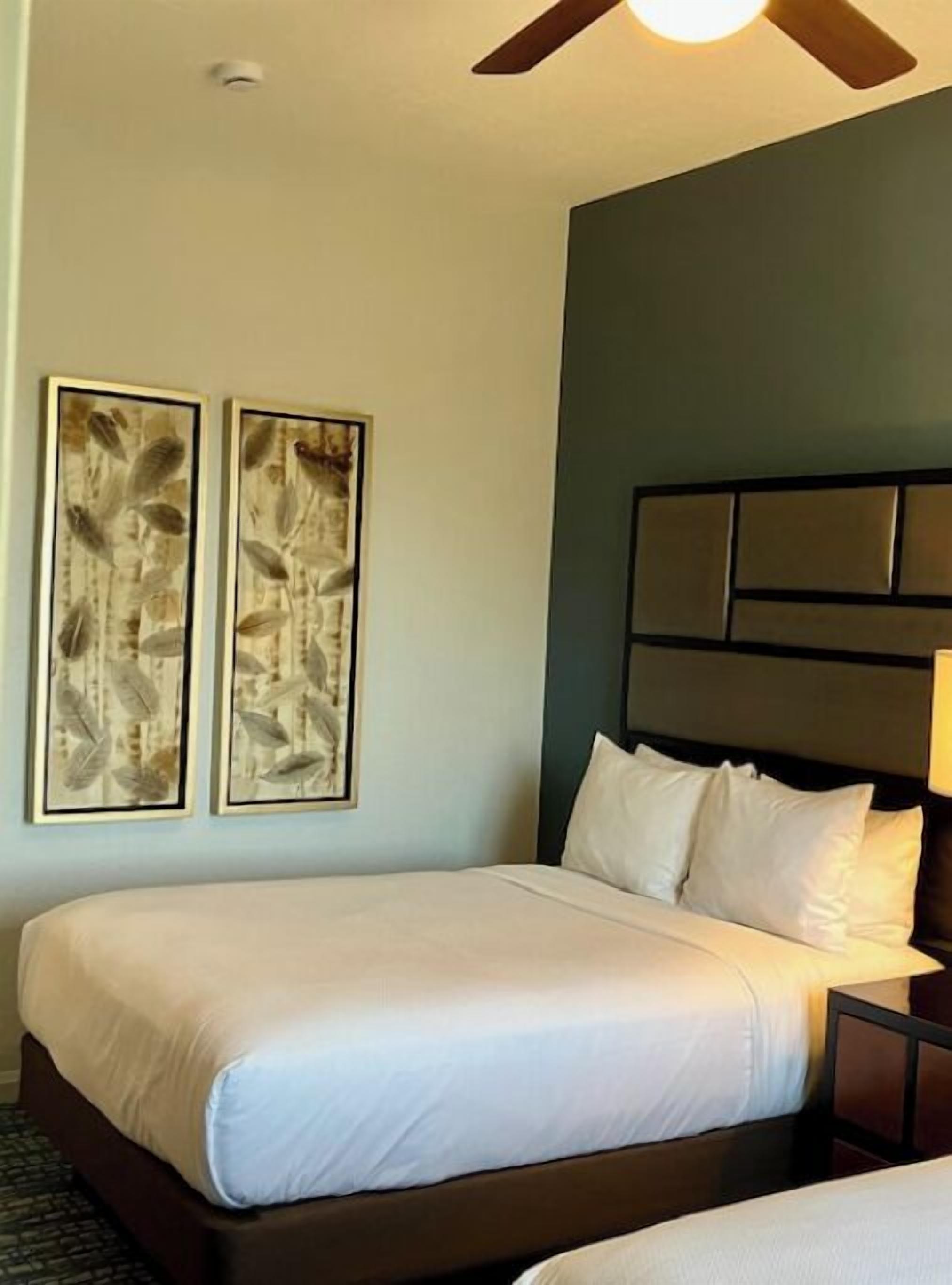 Habitación de hotel con una cama grande, cabecera con varios paneles y dos obras de arte enmarcadas en la pared.