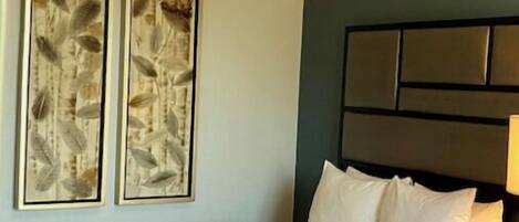 Habitación de hotel con una cama grande, cabecera con varios paneles y dos obras de arte enmarcadas en la pared.