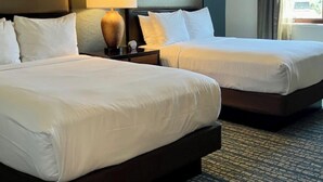 A hotel room with two beds, a nightstand, a lamp, and a view of the outdoors.
