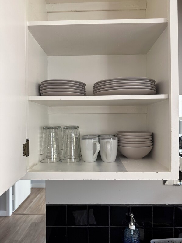 Un mueble de cocina con estantes que sostienen platos, tazones y cristalería.