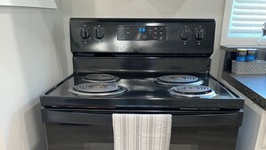 Una estufa Whirlpool negra con cuatro hornillas, un reloj digital y una puerta de horno de acero inoxidable.