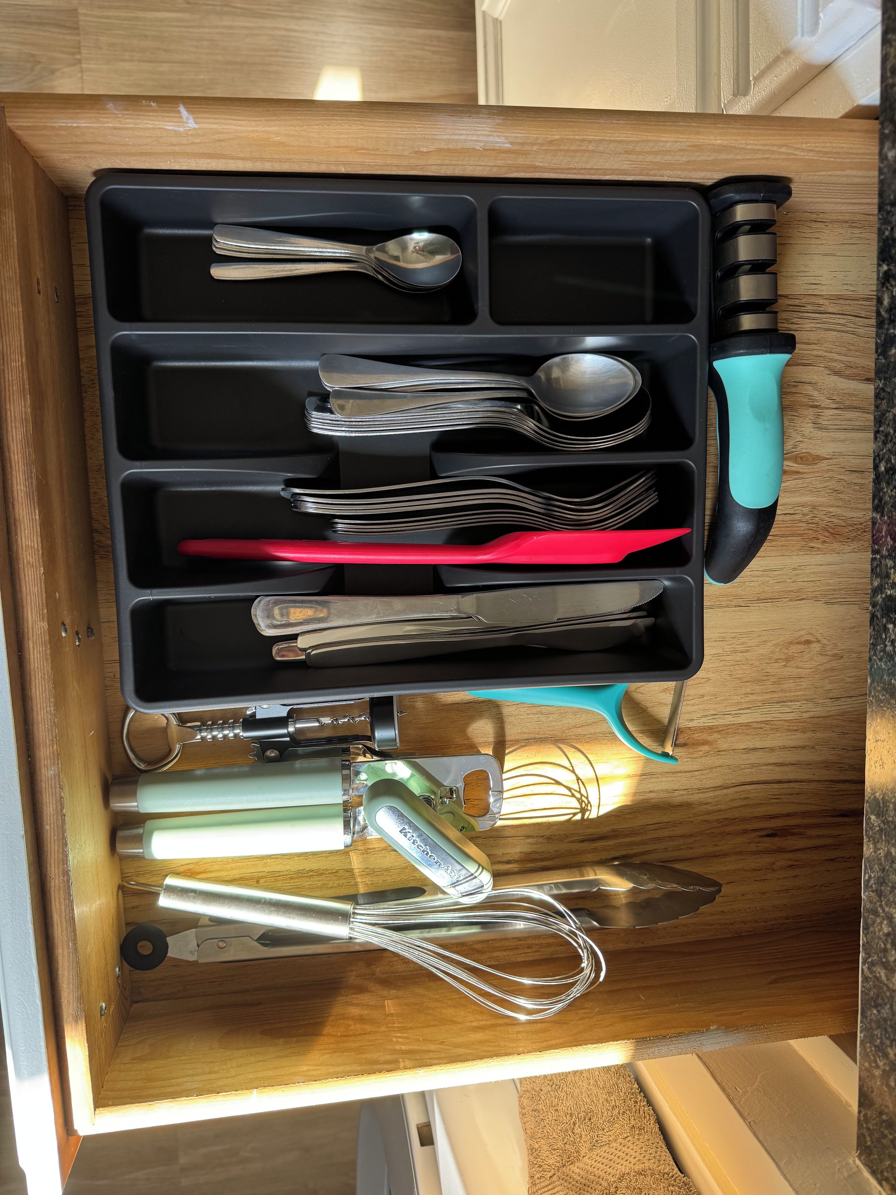 A drawer with kitchen utensils including spoons, forks, a knife, and a whisk.