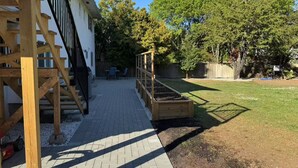 Un patio trasero con terraza de madera, un jardín elevado y césped.