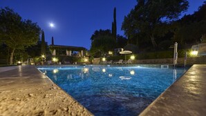 Una piscina al anochecer rodeada de árboles y un pabellón.
