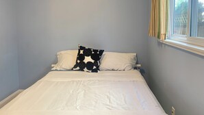 Un lit simple avec une literie blanche et un oreiller à motifs noir et blanc, une fenêtre avec des rideaux et un mur bleu clair.