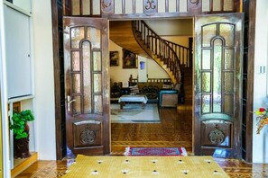 A wooden door with intricate carvings, leading to a room with patterned flooring and a staircase.