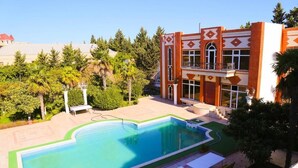 A swimming pool with a geometric design, surrounded by a landscaped area with palm trees and a building with a distinctive architectural style. - Premier Villas (Baku)